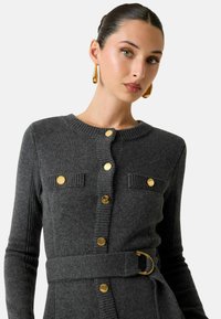 Cardigan grigio lavorato a maglia con scollo rotondo, bottoni dorati, dettagli a coste, tasche sul petto e cintura in tessuto con fibbia dorata.