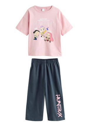 Pink short-sleeve shirt with colorful cartoon characters and "K-POP DEMON HUNTERS HUNTRAX" text, paired with dark gray elastic waist shorts.