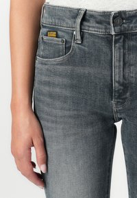 Jeans in denim grigio con finitura sbiadita, design a cinque tasche e accessori metallici neri. Etichetta gialla G-Star sulla tasca anteriore.