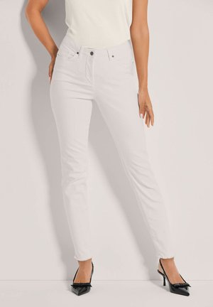 Witte skinny jeans met een hoge taille, licht gescheurde zoom en metalen knoopsluiting, gecombineerd met zwarte puntige hakken.