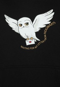 Czarna bluza z kapturem z białą ilustracją sowy trzymającej list. Napis brzmi "CZEKAM NA SWÓJ LIST Z HOGWARTS" w kolorze złotym.