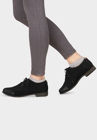 Svarta mocka oxfordskor med utskärningar, rund tå, platt klack och snörning, kombinerade med grå leggings och glittriga strumpor.