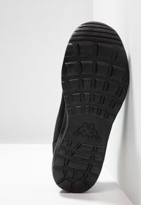 Sola di una scarpa da ginnastica nera con superficie in gomma testurizzata, caratterizzata da motivi a griglia e un dettaglio del logo. Bordo liscio e design della punta arrotondata.