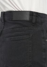 Μαύρο τζιν με απαλό ύφασμα, με δερμάτινο ταμπελάκι στη μέση, πεντα-τσέπη σχεδίαση και διακριτικές ραφές.