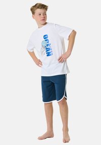 White short-sleeve T-shirt with blue "OCEAN vibes" text and jellyfish graphic; paired with navy blue shorts with white trim.