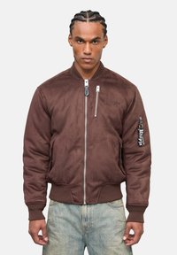 Giacca bomber in suede marrone con polsini e orlo a costine, dotata di una chiusura con zip e tasche laterali. Logo ricamato sulla manica.