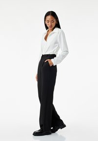Witte lange mouw blouse met een kraag, gecombineerd met hoge zwarte broeken met zijzakken en een relaxed fit. Zwart schoeisel maakt de look compleet.