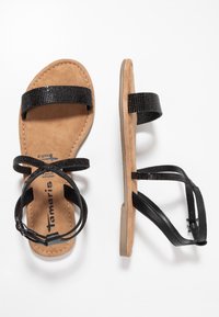Mustat litteät sandaalit, joissa on teksturoidut remmit, pehmustettu beige pohjallinen ja säädettävä nilkkasolki. Neutraalit kumipohjat.