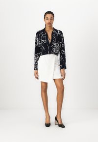 Μαύρο κοντό πουκάμισο με λευκό λουλουδάτο σχέδιο, συνδυασμένο με λευκή φούστα περίτυλης και μαύρες ψηλές γόβες. Λείο ύφασμα, κομμένο σχέδιο.