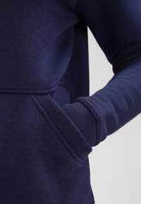 Námořnická modrá mikina s měkkou texturou, se přední kapsou a žebrovanými manžetami. Design obsahuje uvolněný střih a hladké švy.