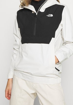 Hvid og sort North Face hættetrøje med frontlynlås, båret af person med hånd i lommen, kombineret med lyse bukser.