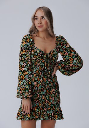 Vestido floral con fondo negro, que presenta flores coloridas en naranja, rosa y azul. Mangas largas abullonadas y dobladillo con volantes.