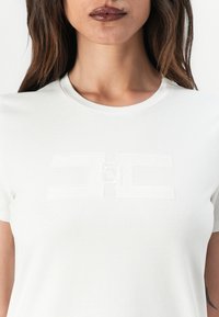 T-shirt en coton blanc avec un logo brodé texturé dans une teinte subtile. Design classique à col ras du cou avec des manches courtes.