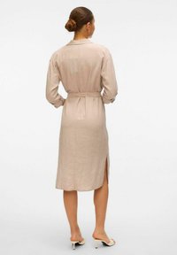 Mauve linneklänning med långa ärmar, bälte i midjan, sprund bak, och knäppta ärmslut, med en krage och knälång design.