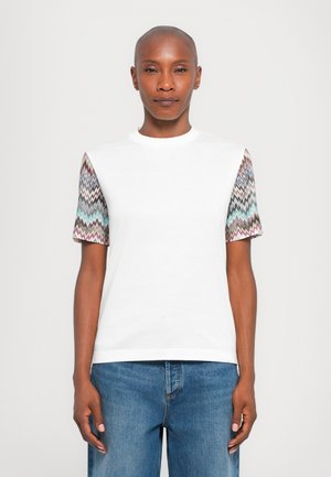 White short-sleeve t-shirt with patterned fabric in zigzag design on sleeves in vibrant colors. Casual fit with round neckline.
