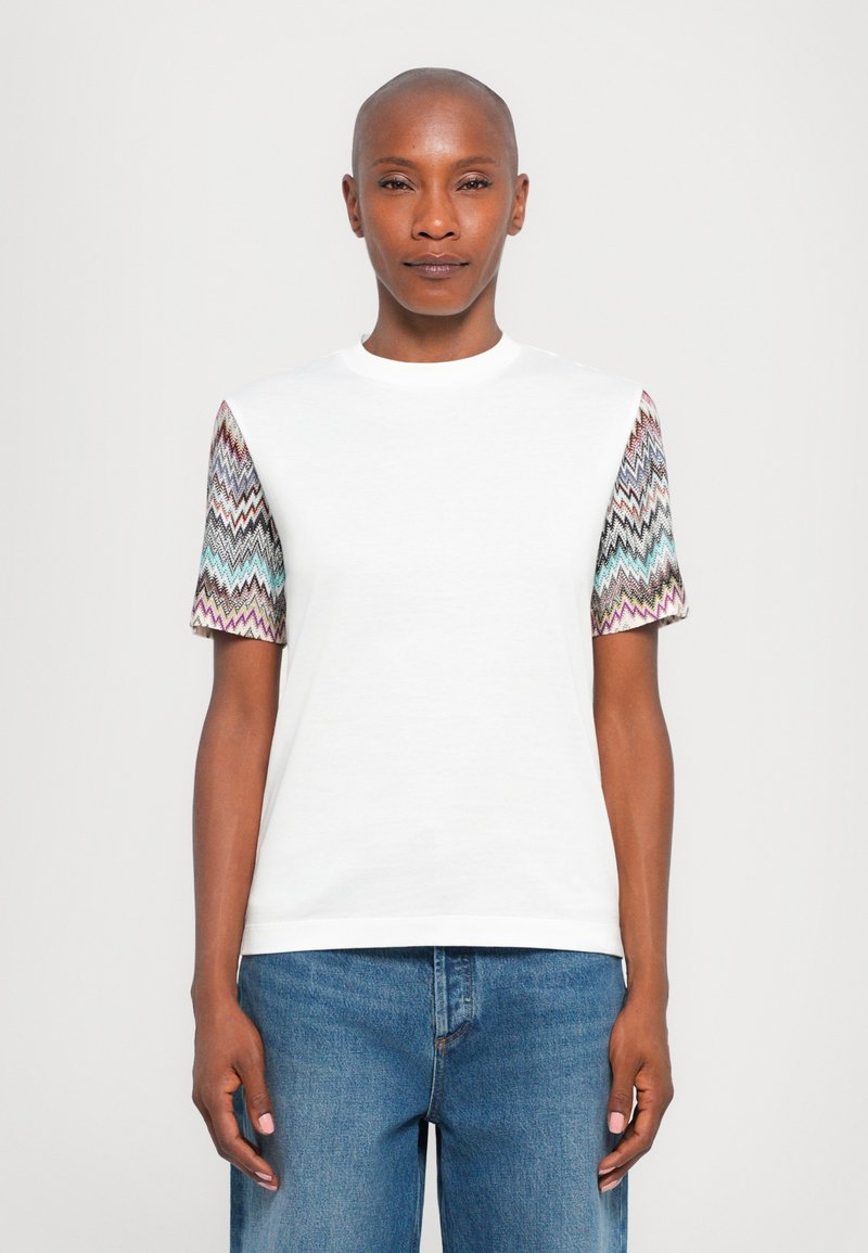 Camiseta blanca de manga corta con tejido estampado en diseño de zigzag en las mangas en colores vibrantes. Corte casual con cuello redondo.