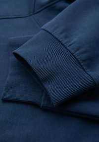 Donkerblauwe sweatshirtstof met ribgebreide boorden, die een gladde textuur en stikseldetail toont. Het ontwerp heeft een eenvoudige, schone esthetiek.