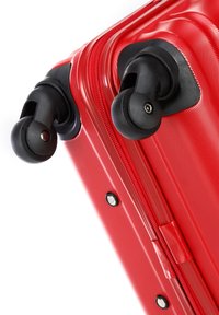 Red hard-shell suitcase featuring textured surface, dual black wheels, sturdy zipper, and reinforced corners for durability.