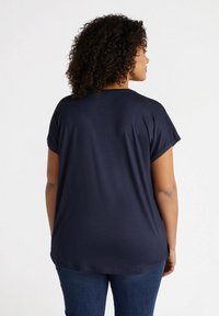 Tricou bleu marin cu mâneci scurte rulate, având o croială lejeră și o textură netedă. Spatele este simplu, cu o margine rotunjită.