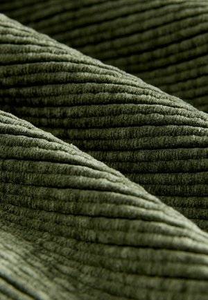 Grüner Cord-Stoff mit ausgeprägten Rillen, der eine weiche Textur und ein geripptes Muster zeigt. Das Material ist plüschig und samtig.