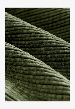 Grüner Cord-Stoff mit ausgeprägten Rillen, der eine weiche Textur und ein geripptes Muster zeigt. Das Material ist plüschig und samtig.