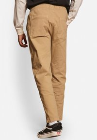 Khaki chinos med en afslappet pasform, elastisk talje, og to baglommer. Kombinationen med sorte skate-sko og hvide sokker.