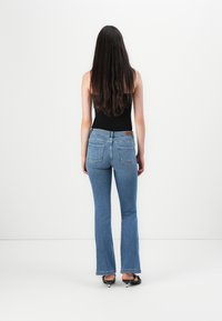 Blå utsvängda jeans med medelhög midja, standardstygn, två bakfickor och en läderlogotyp på den bakre midjebandet.