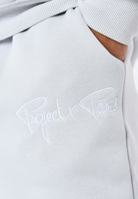 Lichtgrijze sweatstof met een gestructureerd oppervlak en een kangoeroezak; geborduurde "Project x Paris" tekst in het wit op de voorkant.