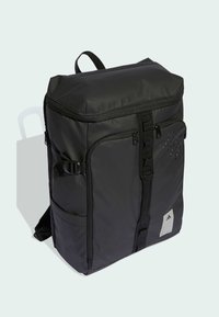 Musta reppu, joka on valmistettu kestävästä kankaasta ja jossa on vetoketjullinen yläosa, säädettävät hihnat, sivutaskut ja rei'itetty muotoiluelementti.