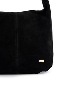 Czarna zamszowa torebka na ramię o miękkiej fakturze, luźnym fasonie, przeszyciach i złotej ozdobie z logo.