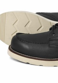 Zapato de cuero negro con suela de goma blanca que presenta un patrón de banda de rodadura en zigzag. Las costuras visibles y un acabado suave realzan su diseño.