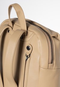 Beige lederen rugzak met een gladde textuur, dubbele bovenhandvatten, ritssluiting en een zijvak met metalen hardware-accenten.