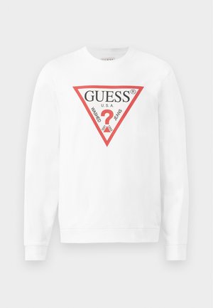 Baltas medvilnės džemperis su dideliu raudonu trikampiu logotipu, kuriame užrašyta "GUESS U.S.A." ir "WASHED JEANS", taip pat su centriniu klausimo ženklo simboliu.