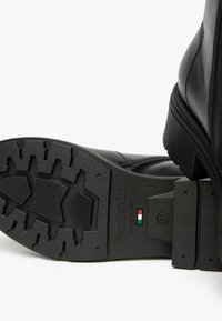 Bottine en cuir noir avec une semelle en caoutchouc texturé arborant un motif de bande de roulement en zigzag. Fermeture éclair et logo embossé sur le côté. Taille 37.
