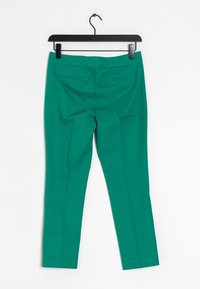 Pantalons tailleur verts avec une texture lisse, comportant deux poches arrière et un design droit élégant, présentés sur un cintre noir.