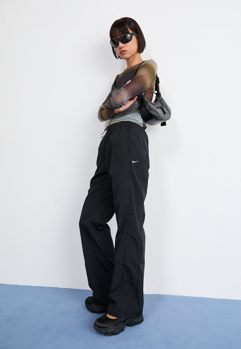 Pantalon noir en nylon avec taille élastique et logo sur le côté ; haut ajusté à manches longues avec dégradé de couleurs ; lunettes de soleil noires surdimensionnées et sac ; chaussures noires chunky.
