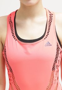 Różowy sportowy top na ramiączkach z czarnymi akcentami, z oddychającą siateczkową strukturą po bokach i logo Adidas z przodu.