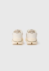 Des chaussures de randonnée beige et crème présentent une tige en daim et en maille, une semelle en caoutchouc épaisse, un col rembourré et un logo embossé au niveau du talon.