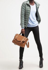 Grøn pufjakke, lyseblå sweater, sorte skinny jeans og sorte hælankelstøvler. Brun skuldertaske med gulddetaljer.