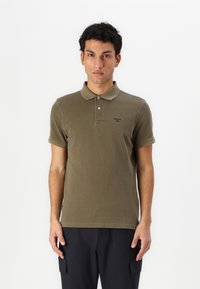 Olivgrünes Poloshirt mit kurzen Ärmeln und einem Kragen, das ein kleines Logo auf der Brust trägt und aus einem weichen, strukturierten Stoff gefertigt ist.