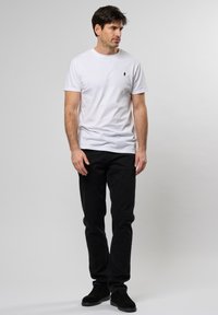 Tricou alb din bumbac, cu guler rotund și un mic logo pe pieptul stâng, asortat cu blugi din denim negri și pantofi din suede negri.