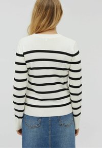 Sweter w paski w kolorze kremowym z czarnymi poziomymi paskami, z okrągłym dekoltem i prążkowanym dołem. Widok od tyłu, noszony z dżinsową spódnicą.