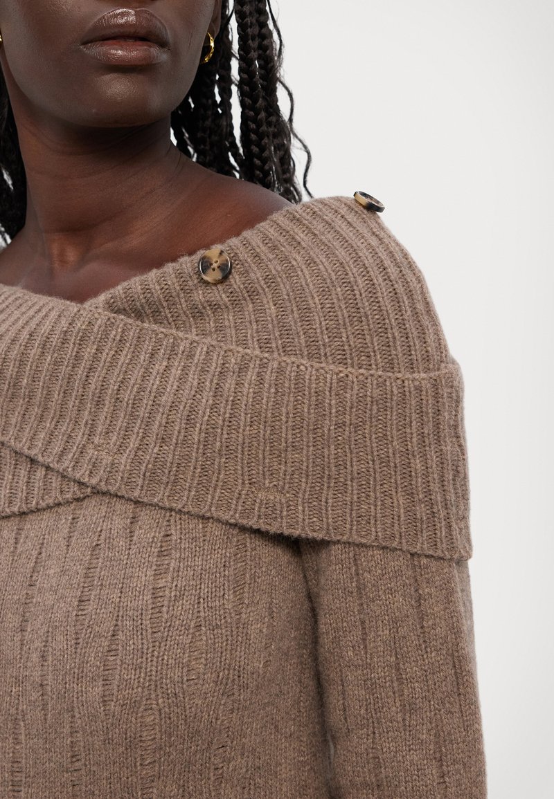 Brauner Strickpullover mit Rippstruktur, schulterfreiem Design und zwei Knöpfen an der Schulter. Verfügt über einen weit geschnittenen Ausschnitt und weichen Stoff.