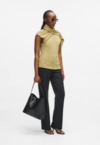 Strikket guld top med draperet udskæring, parret med sorte bukser og en sort lædertaske. Gennemsigtige solbriller og åbne sandaler fuldender looket.