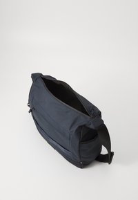 Mørk marineblå budveske med en glatt tekstiloverflate, glidelås-lukking og justerbar stropp. Har kontrasterende blå sømmer og sidepanel.