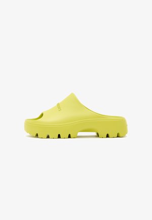 Yellow rubber slide sandal with an open toe, smooth texture, chunky sole, and horizontal grooves for traction. Features a logo on the side.