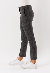 Pantaloni grigi su misura realizzati in tessuto testurizzato, con vestibilità slim, tasche laterali e lunghezza accorciata, abbinati a sneakers bianche.
