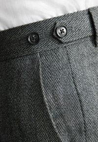Gray herringbone-patterned trousers with dual black buttons at the waist, featuring a textured fabric and sharp pleats for added detail.