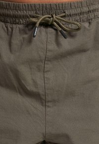 Shorts i et teksturert brunt stoff med elastisk midje, snøring og subtil rutemønster for ekstra detaljer.