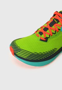 Groene hardloopschoen met een gestructureerd oppervlak, zwarte en turquoise accenten, oranje veters en een gestreept ontwerp op de neus.